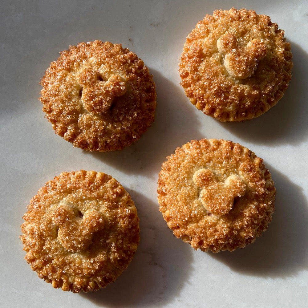 Golden brown, round pies with Mickey Mouse head pie crust decor, sprinkled with raw sugar and sitting on a white counter top.