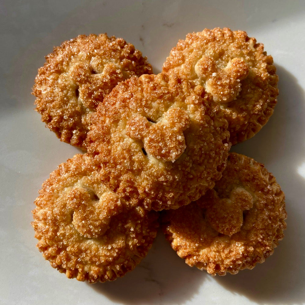 Golden brown, round pie with Mickey Mouse head pie crust decor, sprinkled with raw sugar and sitting on a white counter top. There are five round pies stacked up.