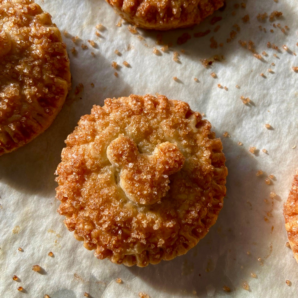 Golden brown, round pies with Mickey Mouse head pie crust decor, sprinkled with raw sugar and sitting on parchment paper.