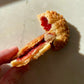 Golden brown, round pie, sprinkled with raw sugar, broken in half to reveal cherry jam inside. A hand holds up one side to reveal the inside. The background is a white counter top. 